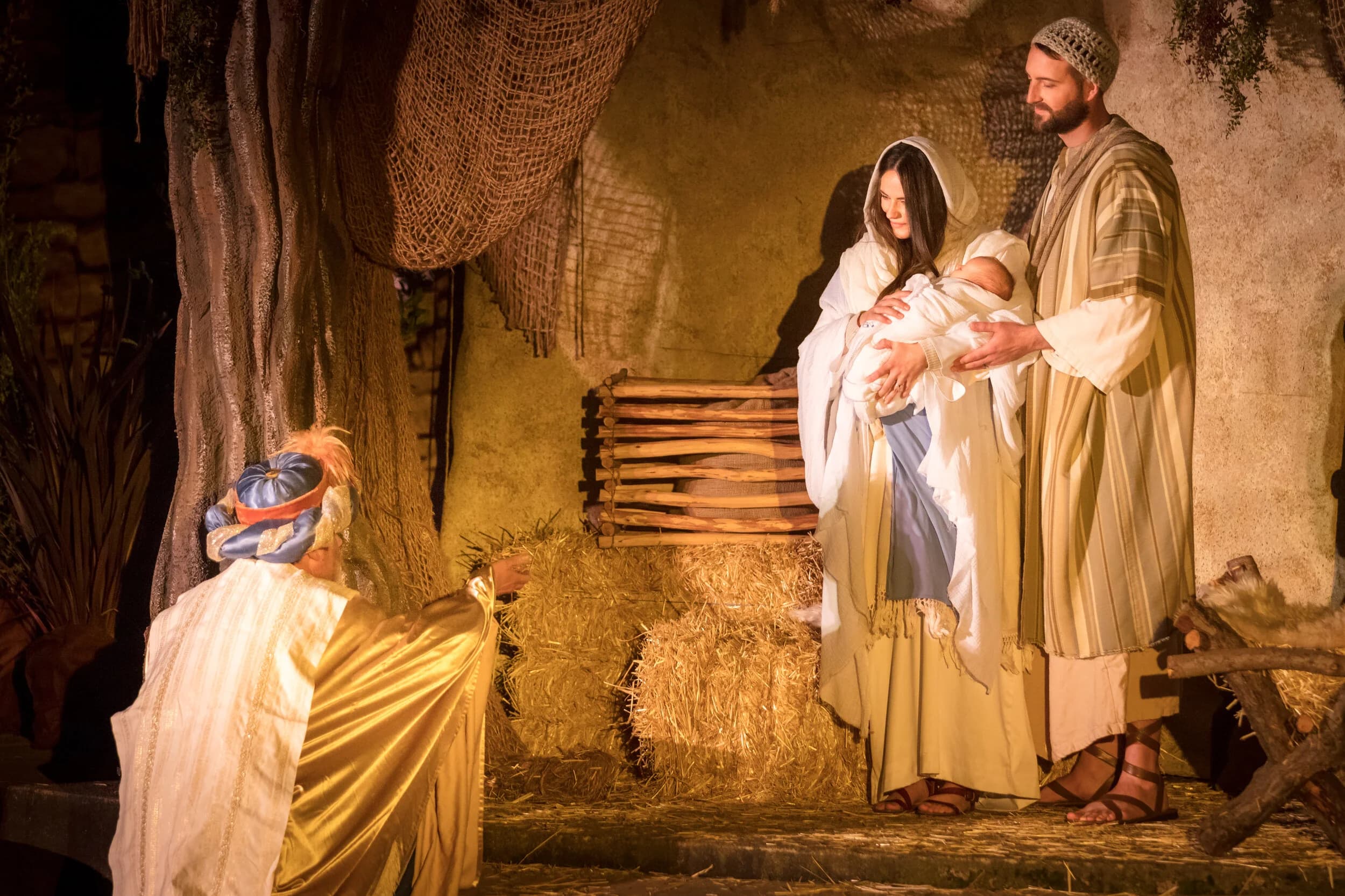 Mary and Joseph present their swaddled newborn to a kneeling wise man in a gold robe inside the stable set.