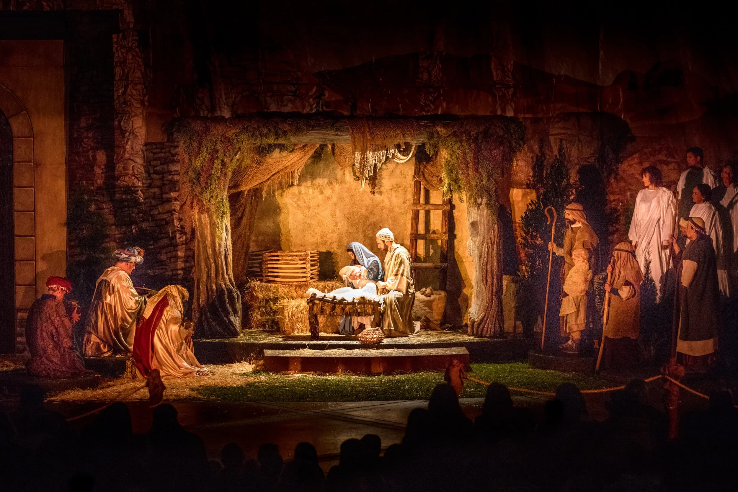 Mary and Joseph kneel beside the manger in a lantern-lit stable while shepherds and townspeople gather around.